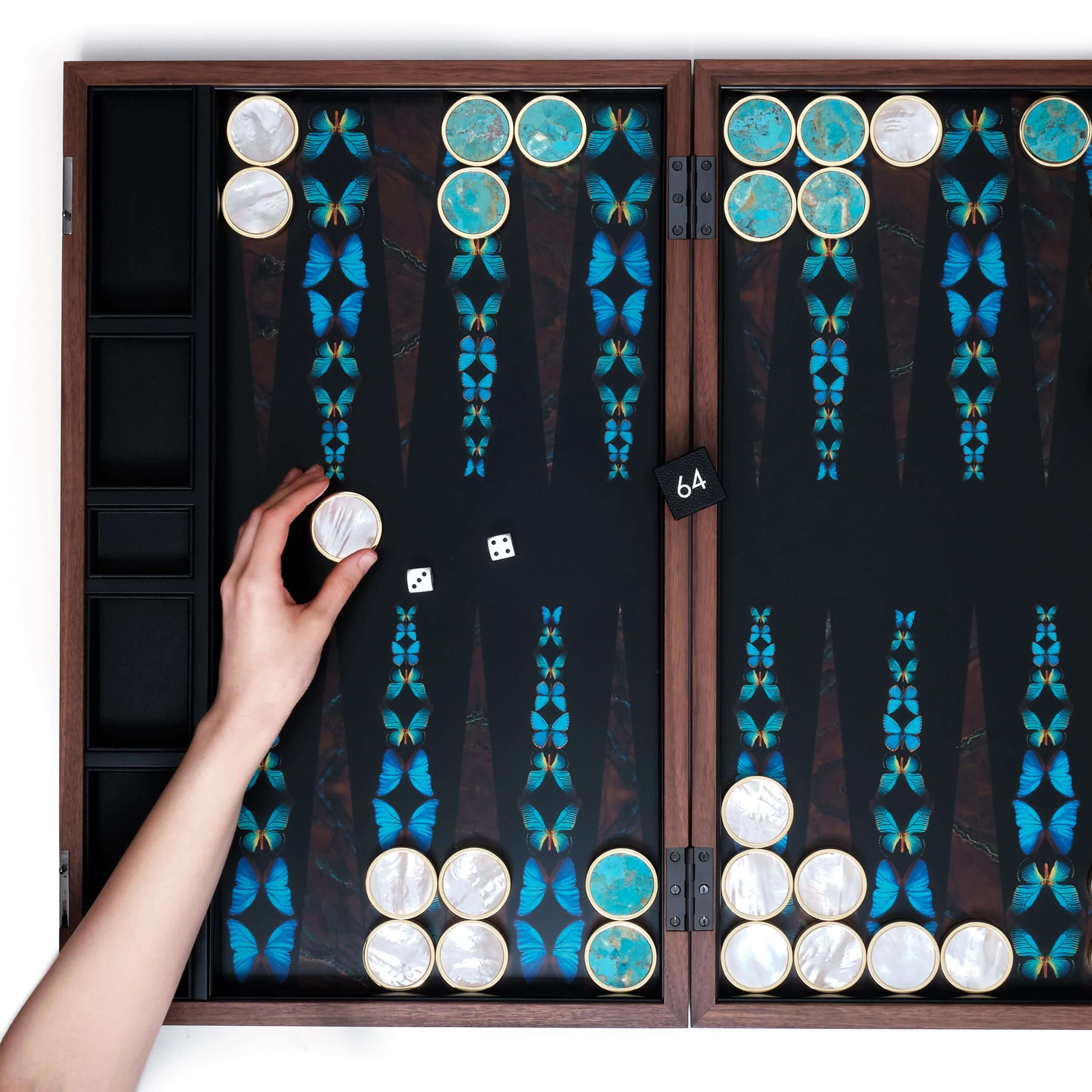 A hand placing a white Mother of Pearl stone and brass playing piece on a Butterfly design backgammon board