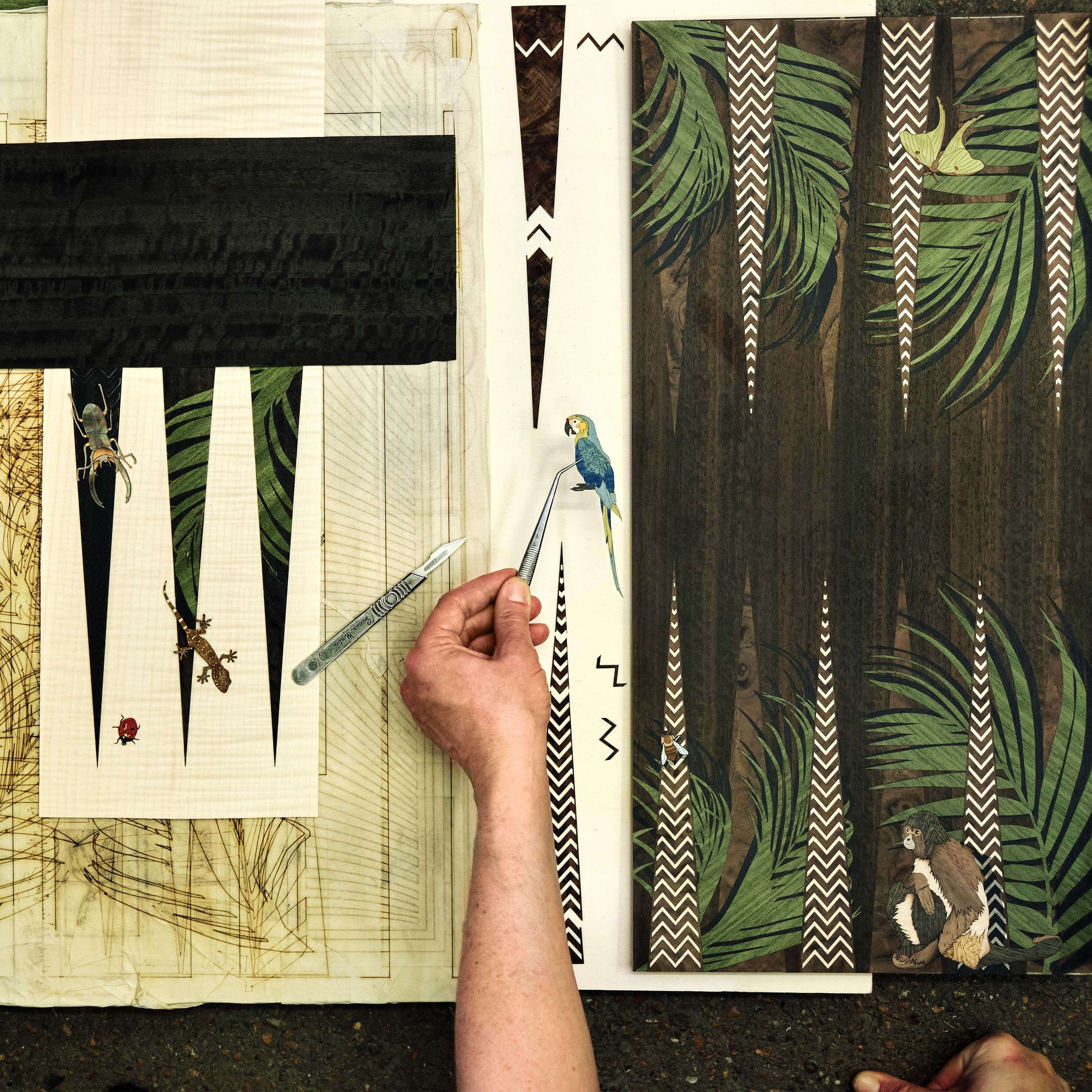 An artist placing a marquetry parrot within a work in progress backgammon board design